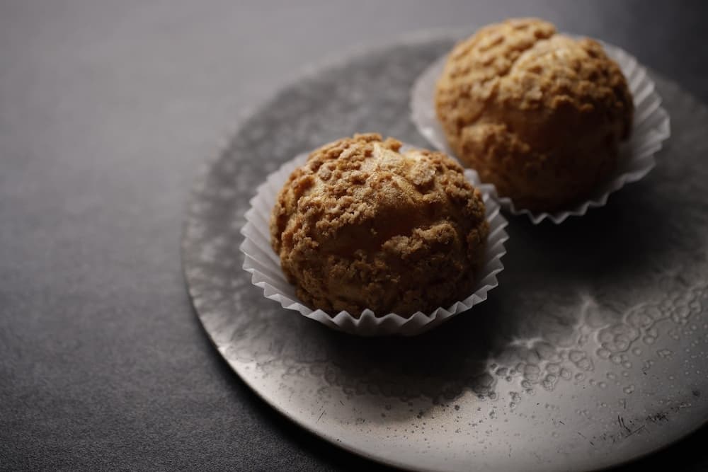 泡芙內餡選用蛋香濃郁的寶玉雞蛋與來自日本頂尖乳品品牌「オーム乳業」的高品質鮮奶油，打造風味濃郁、質地滑順且綿密流動的卡士達醬。為提升香氣層次，特別加入馬達加